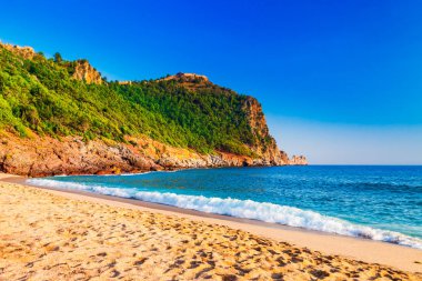 Kleopatra beach Alanya Yarımadası'nda, Antalya bölgesinde, Türkiye'nin yeşil taşlar ile deniz kıyısında. Güzel güneşli manzara ile turizm için temiz su ve kum. Uçurumdaki Alanya Kalesi