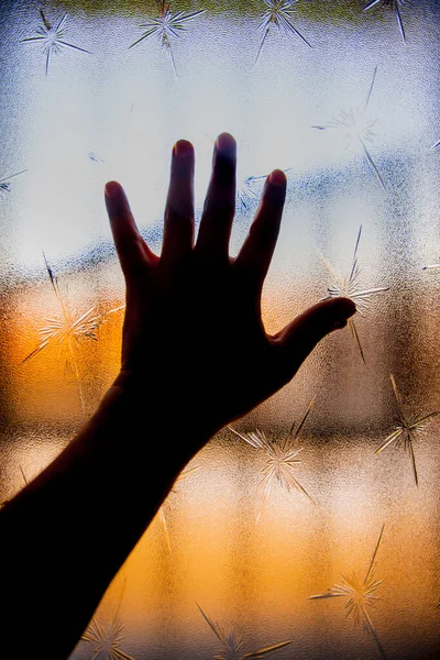 Silhouette of human hand against window glass with color background