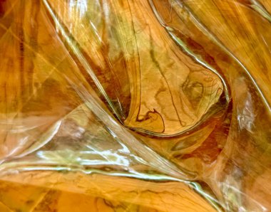 Kahverengimsi renkli ve desenli bir plastik parçası. Plastik katlanmış ve parlak bir yüzeyi var.