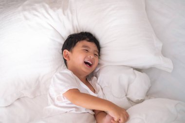 3 yıl eski küçük şirin Asyalı çocuk beyaz gömlek evde yatakta, çocuk oyun yalan ve beyaz yatak yastık ve battaniye ile gülümseyen, kopya alanı olan Üstten Görünüm Ekle metin.