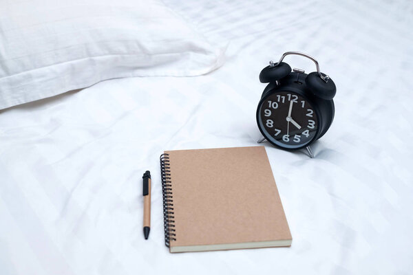 Diary or notebook and vintage alarm clock on bed in bedroom at home or hotel, working or note something before sleep.