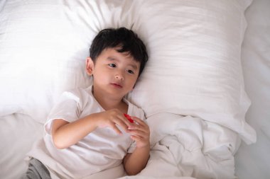 3 yıl eski küçük şirin Asyalı çocuk beyaz gömlek evde yatakta, çocuk oyun yalan ve beyaz yatak yastık ve battaniye ile gülümseyen, kopya alanı olan Üstten Görünüm Ekle metin.