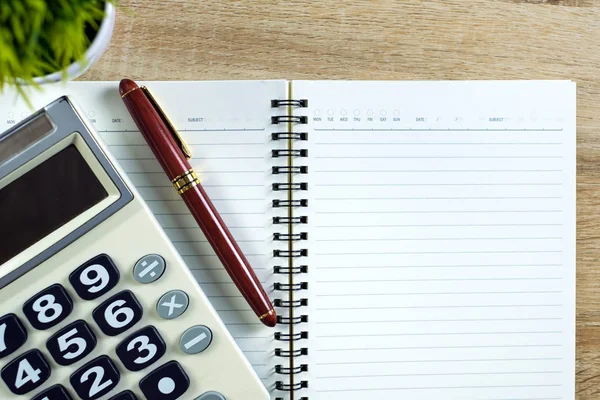 Fountain pen or ink pen with notebook paper and calculator on wooden working table with copy space, office desk concept idea. top view.