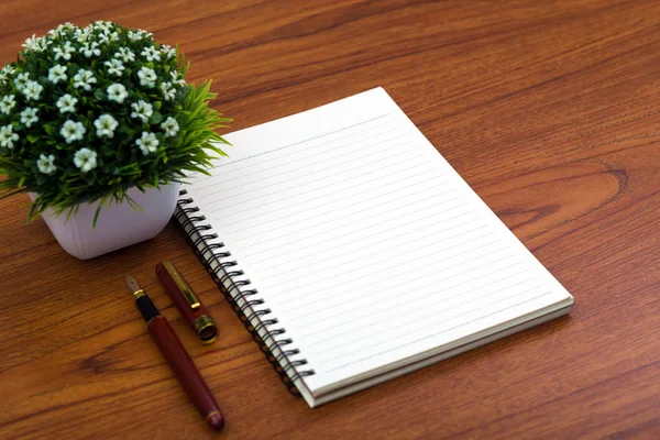 Fountain pen or ink pen with notebook paper and little decoration tree in white vase on wooden working table with copy space, office desk concept idea.