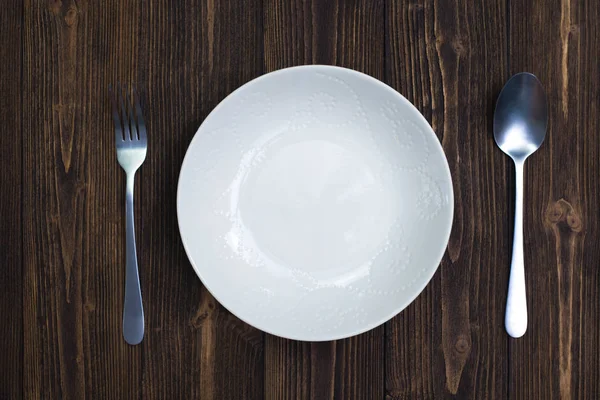 Boş levha veya beyaz tabak kaşık ve çatal ahşap masa, arka plan ve doku, kavram yeme üstten görünüm.