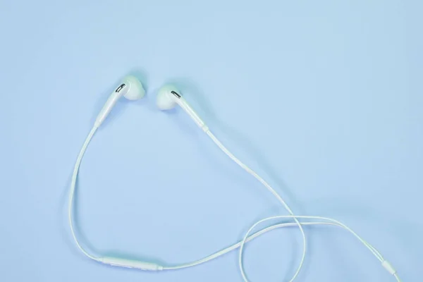 White Earphones or ear buds small talk on sweet blue colour pastel paper, top view, texture and background. music listening concept idea.