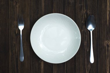 Boş levha veya beyaz tabak kaşık ve çatal ahşap masa, arka plan ve doku, kavram yeme üstten görünüm.