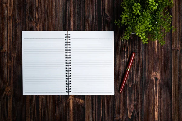 Fountain pen or ink pen with notebook paper and little decoration tree in white vase on wooden working table with copy space, office desk concept idea. top view.