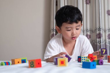 3 yıl eski küçük şirin Asyalı çocuk oynamak oyuncak ya da kare blok bulmaca evde yatakta, yalan blok şekli veya parçalar, eğitim ve sağlıklı kavramı oynayarak öğrenmek.