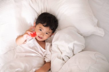 3 yıl eski küçük şirin Asyalı çocuk beyaz gömlek evde yatakta, çocuk oyun yalan ve beyaz yatak yastık ve battaniye ile gülümseyen, kopya alanı olan Üstten Görünüm Ekle metin.