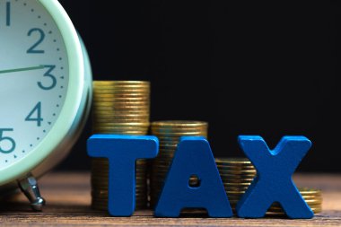 Vergi kavramı ödeme zamanı. Sikke ve vintage çalar saat koyu arka plan, iş ve finansal kavram fikir ahşap çalışma masa yığını ile alfabe vergi.