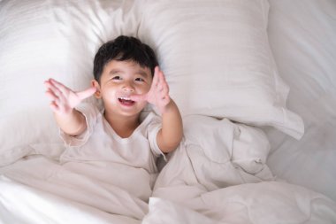 3 yıl eski küçük şirin Asyalı çocuk beyaz gömlek evde yatakta, çocuk oyun yalan ve beyaz yatak yastık ve battaniye ile gülümseyen, kopya alanı olan Üstten Görünüm Ekle metin.