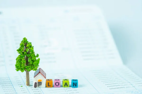 LOAN text and small model house and little tree with notebook, savings banking, loan for house and real estate concept idea.