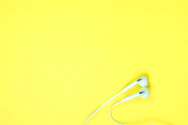 Sohbet tatlı sarı renk pastel kağıt, üstten görünüm, doku ve arka plan üzerinde beyaz kulaklık veya kulak buds. müzik dinleme kavram fikir.
