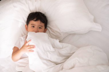 3 yıl eski küçük şirin Asyalı çocuk beyaz gömlek evde yatakta, çocuk oyun yalan ve beyaz yatak yastık ve battaniye ile gülümseyen, kopya alanı olan Üstten Görünüm Ekle metin.