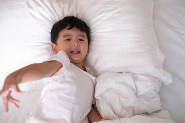 3 yıl eski küçük şirin Asyalı çocuk beyaz gömlek evde yatakta, çocuk oyun yalan ve beyaz yatak yastık ve battaniye ile gülümseyen, kopya alanı olan Üstten Görünüm Ekle metin.