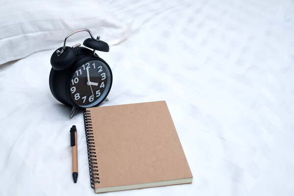 Diary or notebook and vintage alarm clock on bed in bedroom at home or hotel, working or note something before sleep.