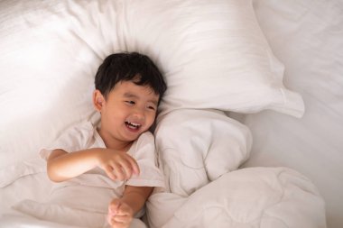 3 yıl eski küçük şirin Asyalı çocuk beyaz gömlek evde yatakta, çocuk oyun yalan ve beyaz yatak yastık ve battaniye ile gülümseyen, kopya alanı olan Üstten Görünüm Ekle metin.