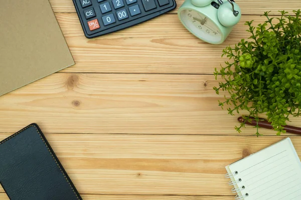 Office supplies or office work essential tools items on wooden desk in workplace, pen with notebook and calculator and alarm clock with copy space, top view