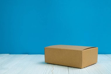 Boş paket kahverengi karton kutu veya tepsi üzerinde parlak beyaz ahşap masa mavi duvar arka plan ile. için kopya alan eklemek metin ya da kelime reklam.