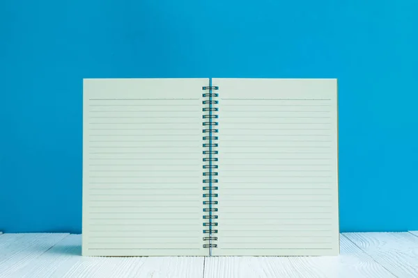 空白笔记本在白色木桌前面蓝色墙壁背景与拷贝空间为添加文本或广告词 菜单样机 — 图库照片