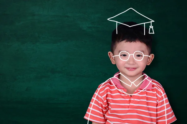 Asian kid imagine his graduated day with hand drawn graduate dress on green chalkboard background, education and graduation concept idea.