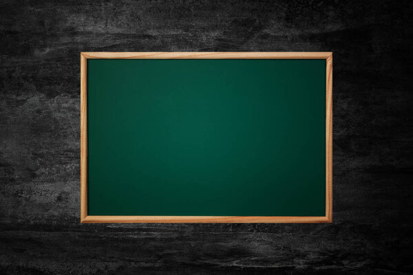 Empty green chalkboard or school board background and texture with wood frame on the black wall, education and back to school concept idea.