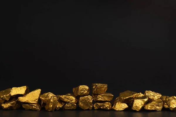 A pile of gold nuggets or gold ore on black background, precious stone or lump of golden stone, financial and business concept idea.