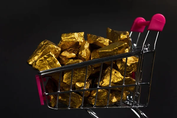 A pile of gold nuggets or gold ore in shopping cart or supermarket trolley on black background, precious stone or lump of golden stone, financial and business concept idea.