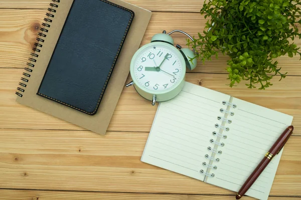 Office supplies or office work essential tools items on wooden desk in workplace, pen with notebook and alarm clock with copy space, top view