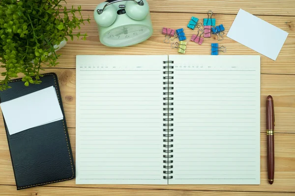 Office supplies or office work essential tools items on wooden desk in workplace, pen with notebook and alarm clock with copy space, top view