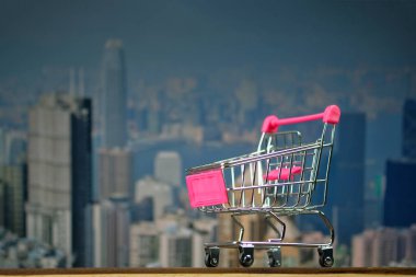 Alışveriş sepeti ya da süpermarket arabası şehir ve arka plan, iş ve finansal kavram fikir ofis binası ile en iyi ahşap çalışma masa üzerinde.