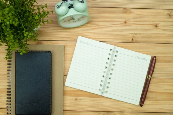 Office supplies or office work essential tools items on wooden desk in workplace, pen with notebook and alarm clock with copy space, top view