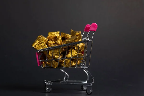 A pile of gold nuggets or gold ore in shopping cart or supermarket trolley on black background, precious stone or lump of golden stone, financial and business concept idea.