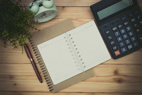 Office supplies or office work essential tools items on wooden desk in workplace, pen with notebook and calculator and alarm clock with copy space, top view