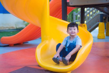 Asyalı çocuk bahçesi yaz, mutlu çocuk anaokulu veya okul öncesi okul bahçesinde ışığında altında slayt oynayan.