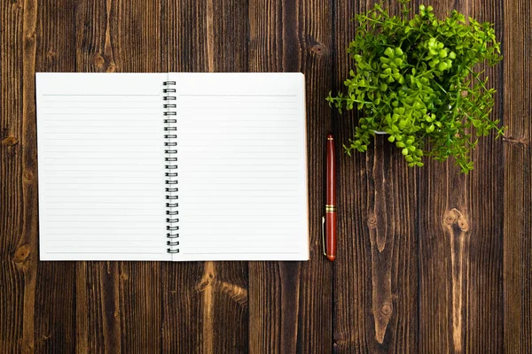 Fountain pen or ink pen with notebook paper and little decoration tree in white vase on wooden working table with copy space, office desk concept idea. top view.