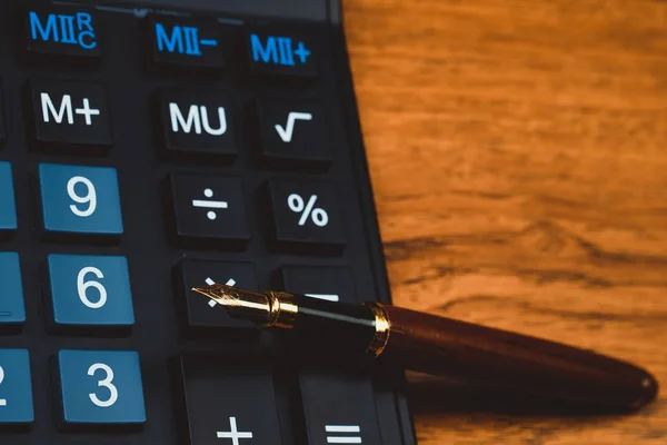 Fountain pen or ink pen with calculator on wooden working table with copy space, office desk concept idea.