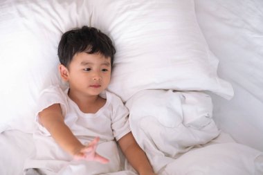 3 yıl eski küçük şirin Asyalı çocuk beyaz gömlek evde yatakta, çocuk oyun yalan ve beyaz yatak yastık ve battaniye ile gülümseyen, kopya alanı olan Üstten Görünüm Ekle metin.