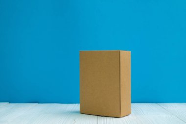 Boş paket kahverengi karton kutu veya tepsi üzerinde parlak beyaz ahşap masa mavi duvar arka plan ile. için kopya alan eklemek metin ya da kelime reklam.