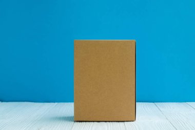 Boş paket kahverengi karton kutu veya tepsi üzerinde parlak beyaz ahşap masa mavi duvar arka plan ile. için kopya alan eklemek metin ya da kelime reklam.