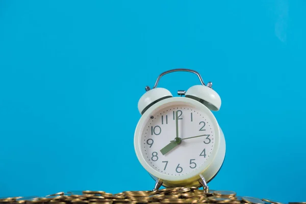 ビンテージの目覚まし時計に青い背景の金のコインの山 時間とビジネス金融コンセプト考え — ストック写真