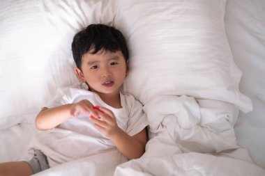 3 yıl eski küçük şirin Asyalı çocuk beyaz gömlek evde yatakta, çocuk oyun yalan ve beyaz yatak yastık ve battaniye ile gülümseyen, kopya alanı olan Üstten Görünüm Ekle metin.