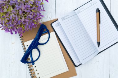 Boş defter kağıt sayfası ve gözlük ile kalem ve ofis malzemeleri, üstten görünüm.