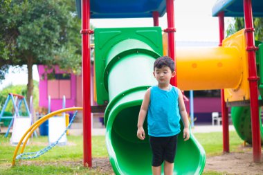 Asyalı çocuk bahçesi yaz, mutlu çocuk anaokulu veya okul öncesi okul bahçesinde ışığında altında slayt oynayan.