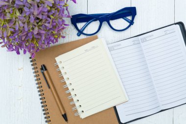 Boş defter kağıt sayfası ve gözlük ile kalem ve ofis malzemeleri, üstten görünüm.
