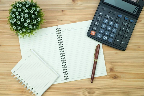 Office supplies or office work essential tools items on wooden desk in workplace, pen with notebook and calculator with copy space, top view