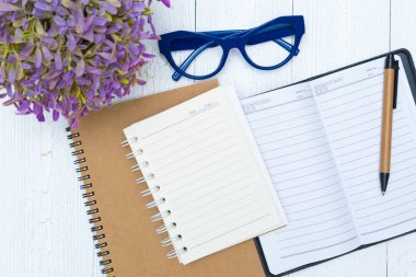 Boş defter kağıt sayfası ve gözlük ile kalem ve ofis malzemeleri, üstten görünüm.