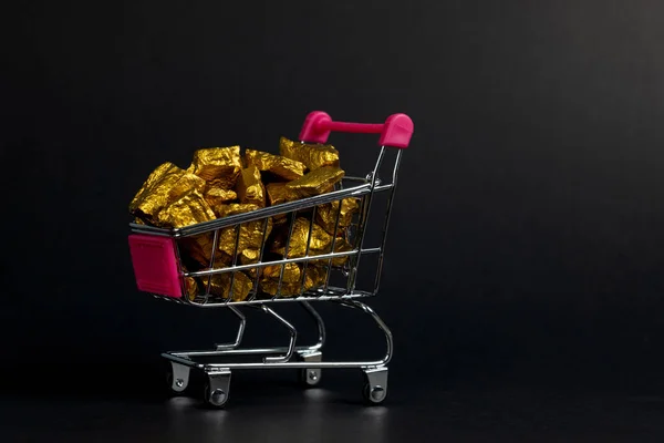 A pile of gold nuggets or gold ore in shopping cart or supermarket trolley on black background, precious stone or lump of golden stone, financial and business concept idea.