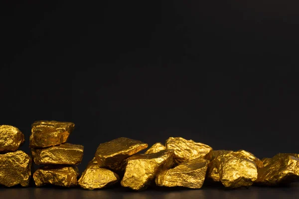 A pile of gold nuggets or gold ore on black background, precious stone or lump of golden stone, financial and business concept idea.